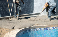 Workers applying concrete around a swimming pool